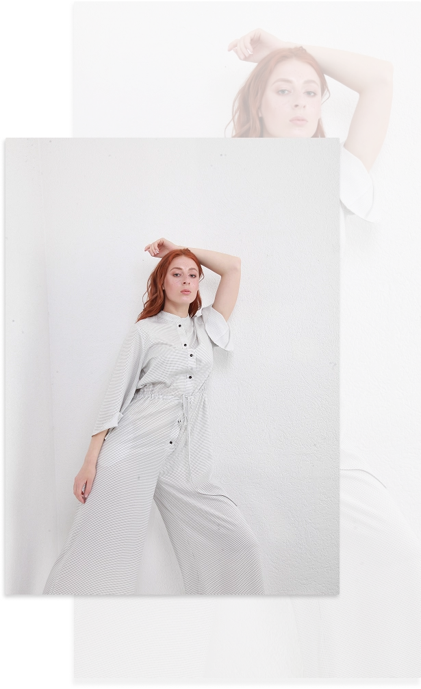 Parlak stüdyo ortamında minimalist beyaz tulum giymiş kızıl saçlı kadın moda portresi.