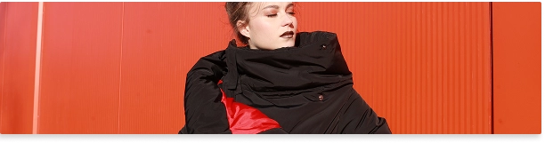 Canlı kırmızı arka plan önünde büyük siyah ve kırmızı ceket giymiş kadın moda portresi.