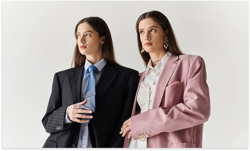 Siyah ve pembe moda stilinde büyük beden iş takımları giymiş iki kadın.